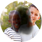 Two young boys are standing together and smiling. A dark, blurry spot in the center of the image blocks part of their faces and bodies.
